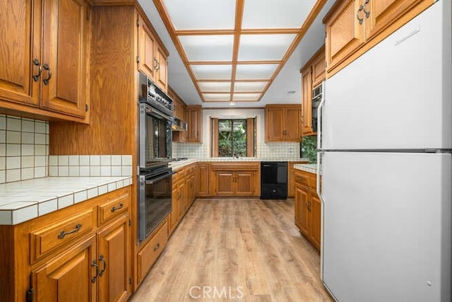 kitchen featuring brown cabinets, tile countertops, decorative backsplash, light wood-type flooring, and black appliances