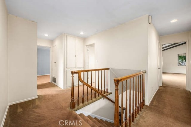 hallway featuring visible vents, baseboards, an upstairs landing, and carpet