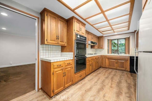 kitchen with dobule oven black, freestanding refrigerator, tile countertops, brown cabinets, and tasteful backsplash