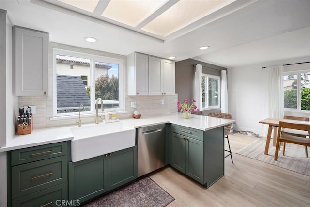 kitchen featuring a breakfast bar, a sink, a peninsula, stainless steel dishwasher, and green cabinets