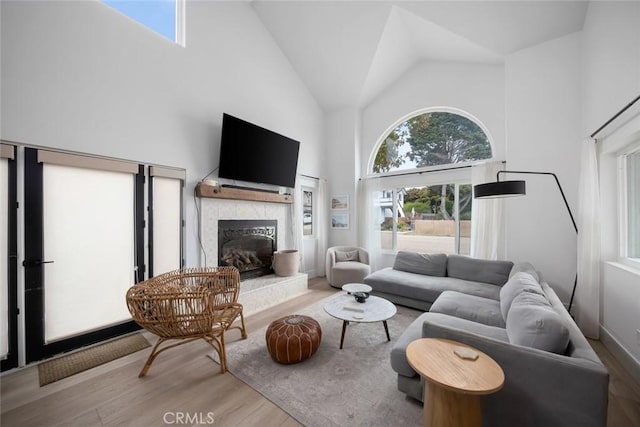 living room featuring wood finished floors, a wealth of natural light, high vaulted ceiling, and a tile fireplace