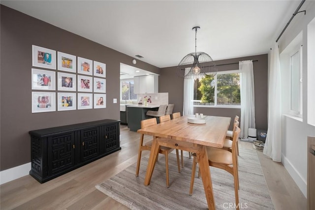 dining space with baseboards, a notable chandelier, visible vents, and light wood-style floors