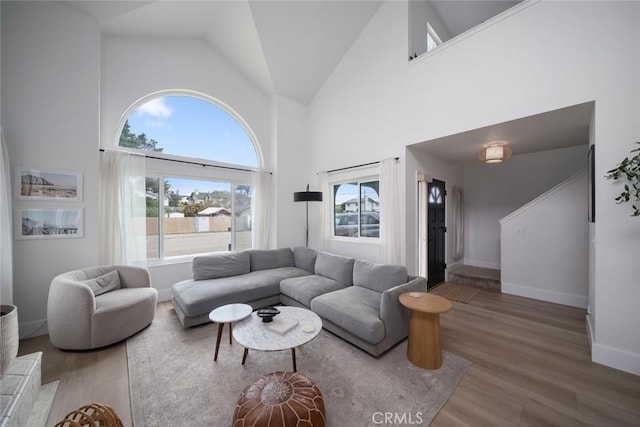 living area with baseboards, wood finished floors, and high vaulted ceiling