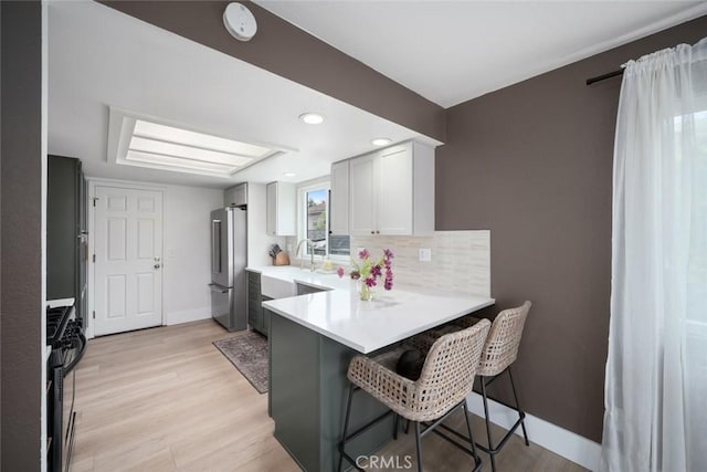 kitchen featuring black gas range, freestanding refrigerator, a kitchen breakfast bar, light countertops, and tasteful backsplash
