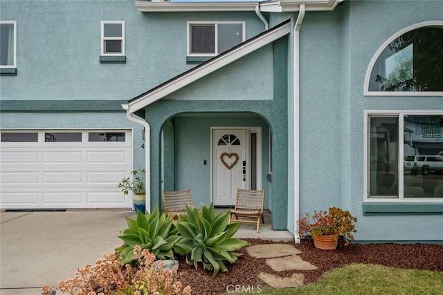 doorway to property with an attached garage, driveway, and stucco siding