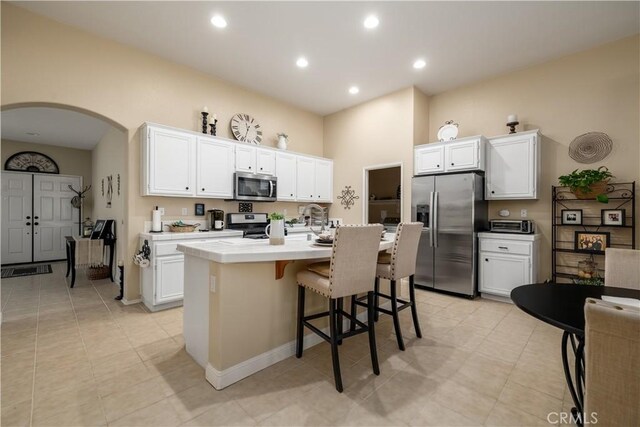 kitchen featuring arched walkways, white cabinets, stainless steel appliances, and a center island with sink