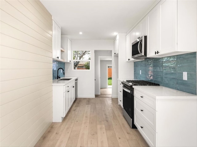 kitchen with open shelves, a sink, light countertops, light wood finished floors, and stainless steel appliances
