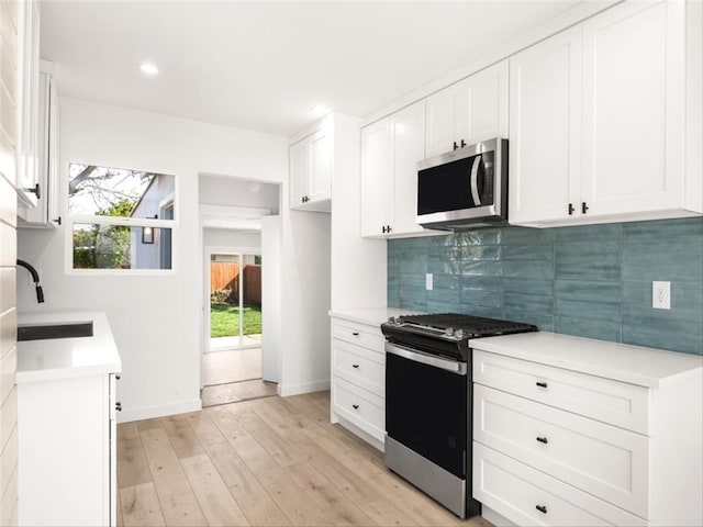 kitchen with a sink, light wood-style floors, light countertops, stainless steel appliances, and decorative backsplash