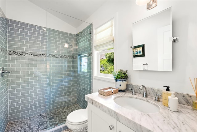 bathroom with vanity, vaulted ceiling, a tile shower, and toilet