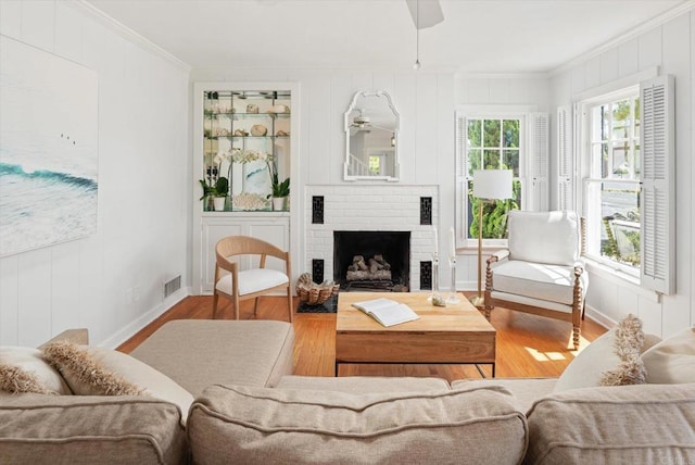 living room featuring crown molding, visible vents, a brick fireplace, and wood finished floors