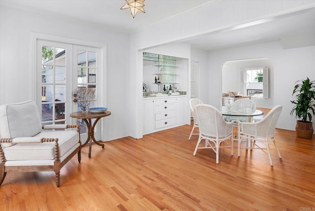 dining room featuring arched walkways, ornamental molding, a healthy amount of sunlight, and light wood-style flooring