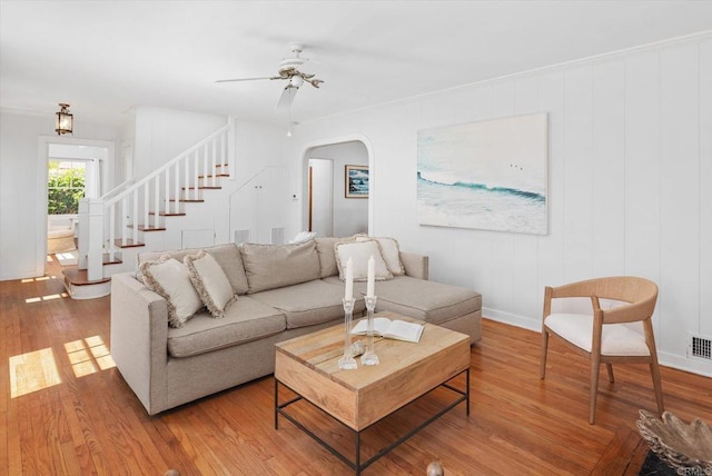 living room with a ceiling fan, arched walkways, wood finished floors, baseboards, and stairs