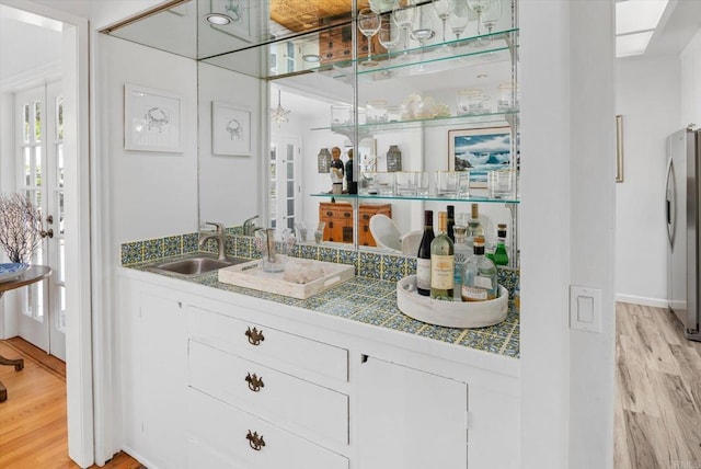 bar with a sink, freestanding refrigerator, and light wood-type flooring