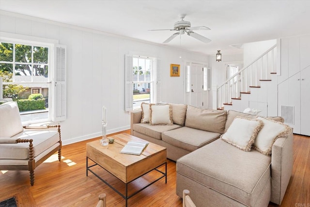 living room featuring light wood-style floors, baseboards, stairway, and a ceiling fan