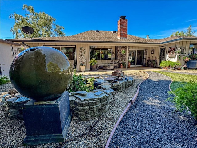 back of property with board and batten siding, a chimney, a patio area, an outdoor fire pit, and a shingled roof