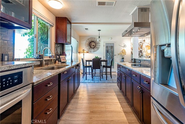 kitchen with wall chimney range hood, visible vents, appliances with stainless steel finishes, light wood-type flooring, and a sink