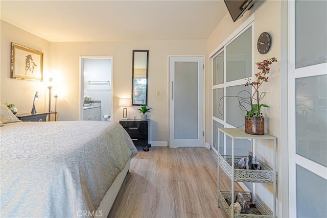 bedroom with connected bathroom, baseboards, and wood finished floors