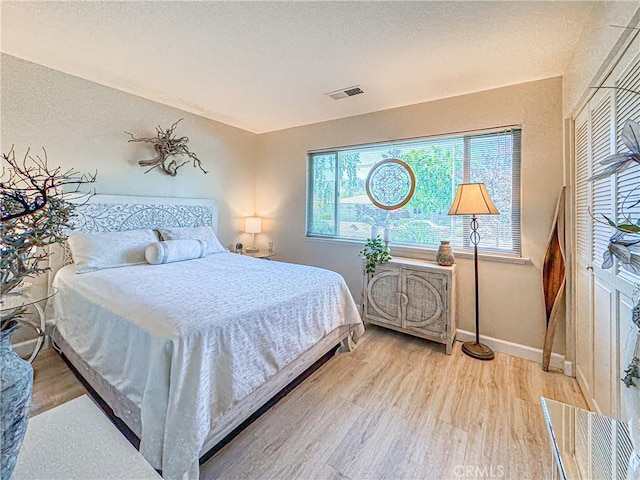 bedroom featuring visible vents, a textured ceiling, baseboards, and wood finished floors