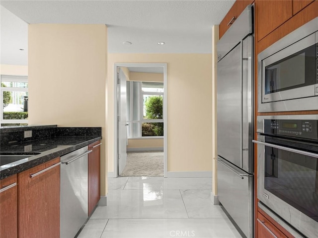 kitchen featuring plenty of natural light, brown cabinetry, dark stone countertops, and built in appliances