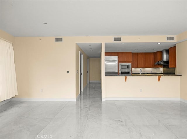kitchen featuring visible vents, dark countertops, built in appliances, and wall chimney range hood