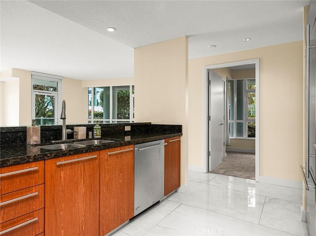 kitchen with stainless steel dishwasher, marble finish floor, dark stone counters, brown cabinets, and a sink