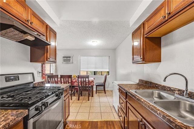 kitchen with a wall unit AC, dark countertops, a sink, stainless steel range with gas cooktop, and under cabinet range hood