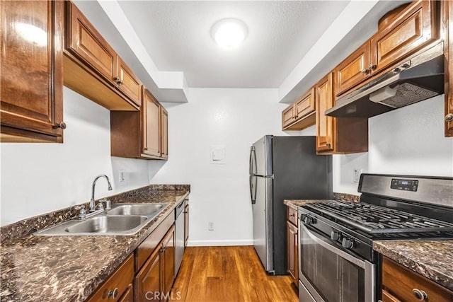kitchen with dark wood-style flooring, baseboards, under cabinet range hood, a sink, and stainless steel appliances