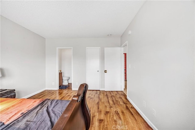 bedroom with baseboards, a textured ceiling, light wood finished floors, and ensuite bath