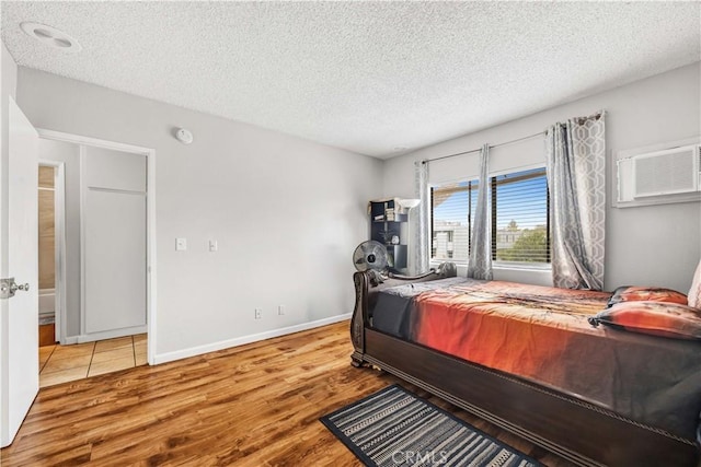 bedroom featuring a textured ceiling, baseboards, a wall mounted air conditioner, and wood finished floors