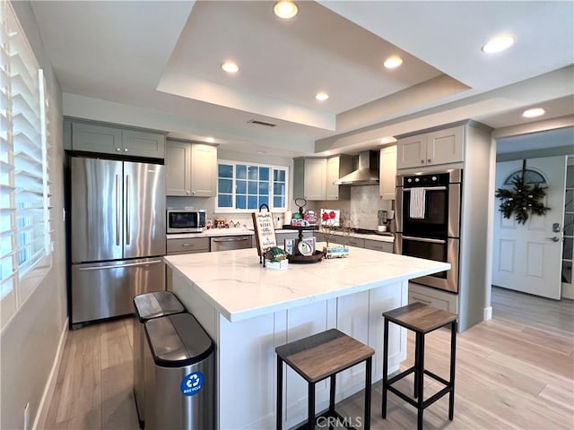 24052 Estacia Ave, Laguna Niguel, CA 92677 - kitchen featuring wall chimney range hood, light wood-type flooring, gray cabinets, a tray ceiling, and stainless steel appliances
