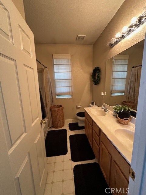 full bath with visible vents, a sink, a textured ceiling, and toilet