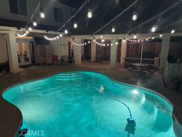pool at twilight with fence, french doors, a fenced in pool, a patio area, and a hot tub