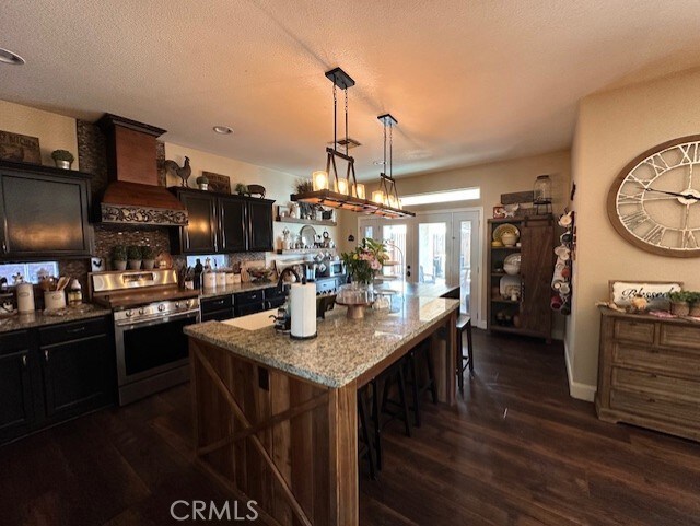 kitchen featuring stainless steel electric range oven, dark wood-style flooring, light stone countertops, a breakfast bar, and custom range hood