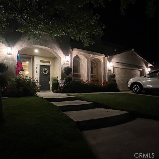 view of front of property with an attached garage, a lawn, and stucco siding