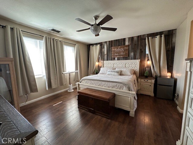bedroom featuring dark wood finished floors, baseboards, wood walls, and visible vents