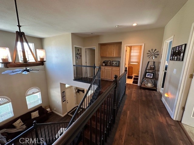 corridor with a chandelier, an upstairs landing, dark wood-style floors, and a wealth of natural light