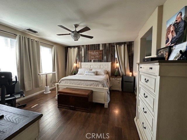 bedroom with wooden walls, a ceiling fan, visible vents, and dark wood-type flooring