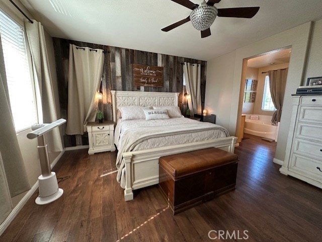 bedroom featuring wood walls, baseboards, dark wood-style floors, connected bathroom, and a ceiling fan