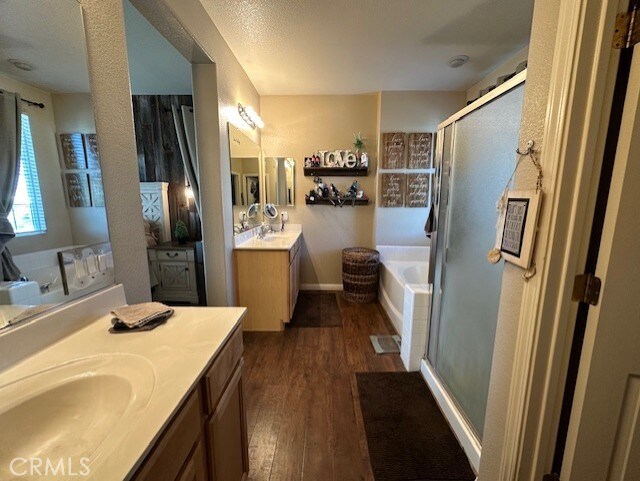 bathroom with a bath, a stall shower, two vanities, a sink, and wood-type flooring