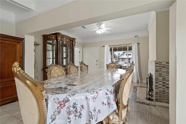 dining area featuring a tile fireplace, crown molding, visible vents, and ceiling fan