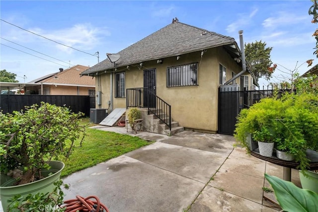 view of front of house featuring a patio, stucco siding, fence, central air condition unit, and roof with shingles
