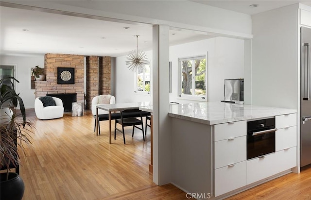 kitchen with white cabinets, light stone counters, black oven, light wood-style flooring, and modern cabinets