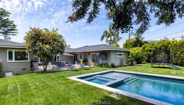 back of property featuring a patio, a trampoline, an in ground hot tub, and stucco siding