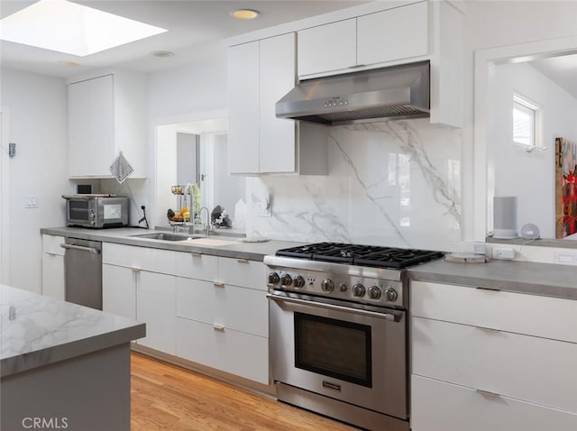 kitchen featuring white cabinets, stainless steel appliances, backsplash, under cabinet range hood, and a skylight