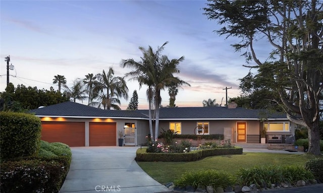 ranch-style house featuring a chimney, a lawn, concrete driveway, an attached garage, and stucco siding