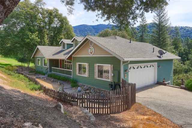 view of front of house with fence, roof with shingles, an attached garage, a mountain view, and driveway