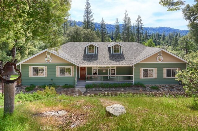 view of front of house with covered porch, a forest view, a mountain view, and roof with shingles