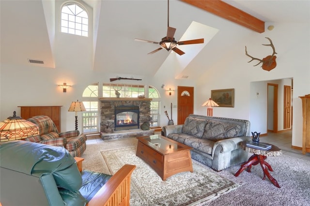 living room featuring ceiling fan, beam ceiling, high vaulted ceiling, a stone fireplace, and visible vents