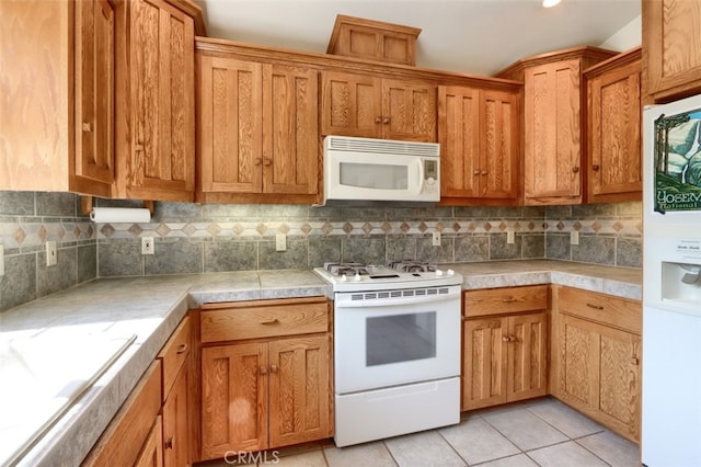 kitchen featuring brown cabinetry, backsplash, light countertops, light tile patterned floors, and white appliances
