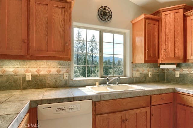 kitchen with brown cabinetry, white dishwasher, light countertops, a sink, and backsplash